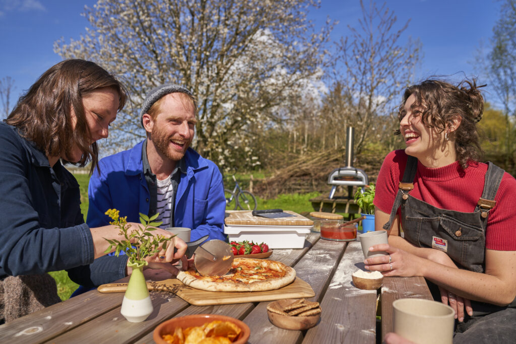 OONI Pizzaofen outdoor – Freunde genießen frische Pizza beim geselligen Essen im Garten