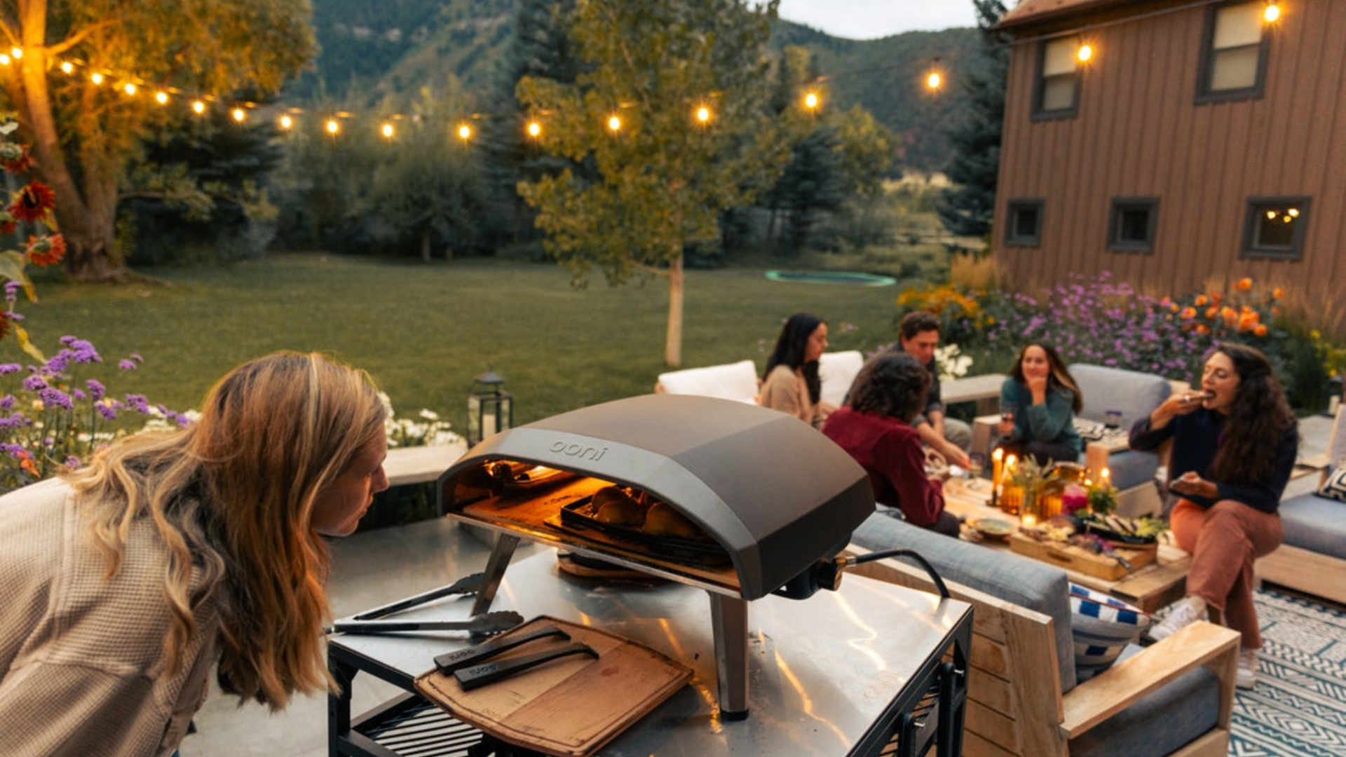 Gruppe von Freunden feiert abendliche Gartenparty mit Ooni Koda 16 Gaspizzaofen und Lichterketten – Pizza Party im Garten