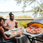 Paar genießt frische Pizza vom Ooni Koda 12 Gas-Pizzaofen auf der Terrasse – Outdoor-Pizzaofen für authentische Steinofenpizza mit Blick ins Grüne