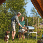 Zwei Personen bereiten mit dem Ooni Karu 12 Pizza im Freien zu – Outdoor-Cooking beim Camping mit Hund