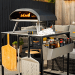 OONI Modultisch Groß komplett bestückt – Koda Pizzaofen mit Flammen, Utensilienfach mit Saucen, Bambus- und Alu-Pizzaschieber auf Terrasse