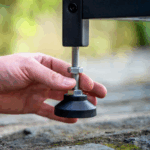 Hand stellt OONI Modular-Tisch Schraubfuß ein – Höhenverstellung des Tischfußes per Hand auf Outdoor-Untergrund