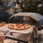 Frisch gebackene Pizza vor dem Ooni Koda 2 Pizzaofen in Dunkelblau mit Rauch im Garten