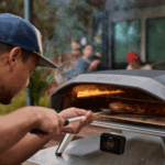 Mann backt Pizza im Ooni Koda 2 Pro Schwarz Gas-Pizzaofen mit integrierter Digitalanzeige im Garten