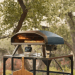 Ooni Koda 2 Pro Dunkelblau Gas-Pizzaofen mit Pizza auf Backstein im Garten auf stabilem Tisch