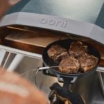 Fleischstücke braten in einer Pfanne im Ooni Koda 2 Pro Dunkelblau Outdoor Pizzaofen