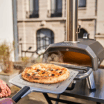 Frisch gebackene, dampfende Pizza auf Pizzaschaufel vor dem Ooni Karu 12 Outdoor-Pizzaofen – authentischer Holzofen-Genuss zu Hause