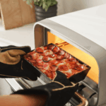 Frisch gebackene Pepperoni-Pizza wird aus dem Ooni Volt 12 in Polareweiß entnommen