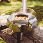 Ooni Holzpizzaofen mit brennenden Eichen-Holzscheiten auf Holztisch im Garten – Outdoor-Pizzaofen mit Flammen