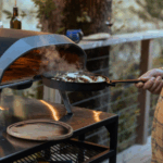 Ooni Grillpfanne aus Gusseisen wird dampfend aus Ooni Pizzaofen gezogen – Kochen im Holzpizzaofen outdoor