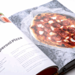 Aufgeschlagene Seite aus dem Ooni Kochbuch "Cooking with Fire" mit Peperoni Pizza Rezept und Foto – Pizzaofen Rezeptbuch mit Schritt-für-Schritt Anleitung