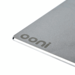 Nahaufnahme der Ooni Pizzabackstahl-Oberfläche mit eingeprägtem Ooni-Logo und abgerundetem Edelstahlrand – matte Textur des hochwertigen Backstahls für gleichmäßige Wärmeverteilung